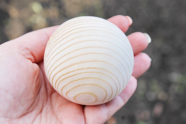 Puede incluir: Primer plano de una bola de madera blanca con c&iacute;rculos conc&eacute;ntricos tallados en la superficie. La bola est&aacute; siendo sostenida en la mano de una persona.