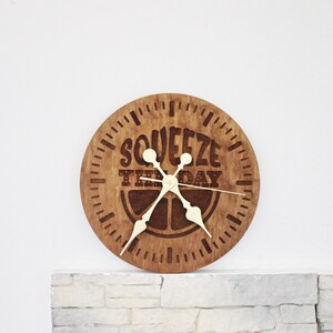 May include: A wooden clock with a brown background and white hands. The clock face has the text "Squeeze the Day" and a stylized lemon design.