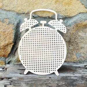 May include: A white wooden alarm clock with a round face and a hole pattern. The clock has a handle on top and two bells on the sides.