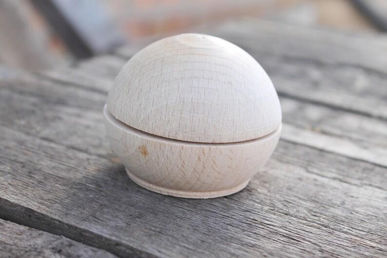 May include: A wooden, round, two-piece box with a smooth, light brown finish. The box is closed and sitting on a wooden surface.