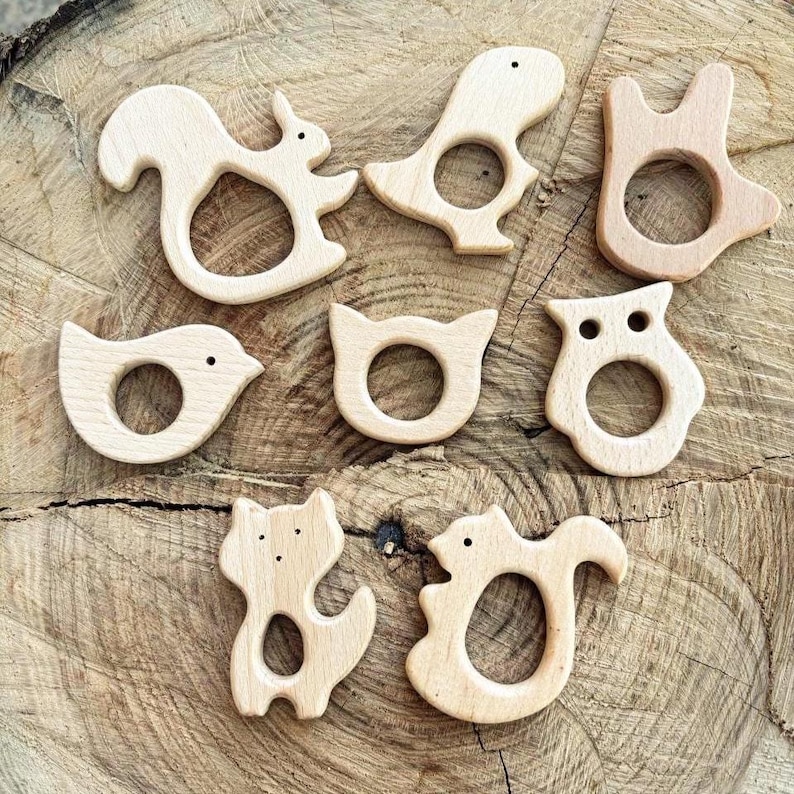 Peut inclure: Ensemble de sept anneaux de dentition en bois pour b&eacute;b&eacute;s, en forme d'animaux : &eacute;cureuil, oiseau, dinosaure, hibou et renard. Chaque jouet est en bois clair et poss&egrave;de une ouverture circulaire pour une prise en main facile. Les jouets sont dispos&eacute;s sur une surface en bois textur&eacute;e.