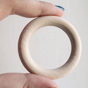May include: A plain, light brown wooden ring, held in a hand.