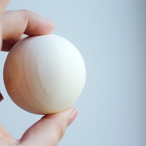 May include: A white wooden sphere with a light brown wood grain pattern.