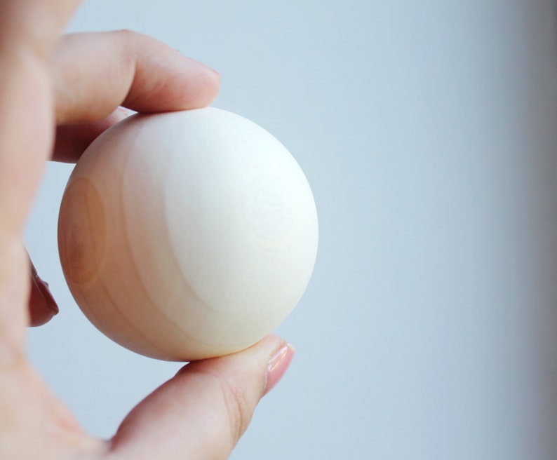 May include: A white wooden sphere with a light brown wood grain pattern.