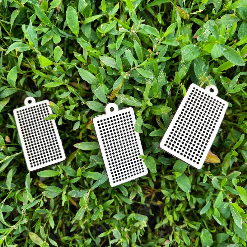 Peut inclure: Trois pendentifs rectangulaires blancs pr&eacute;sentant une grille uniforme de petites perforations circulaires et une boucle d'attache unique sur le dessus. Ces composants plats et g&eacute;om&eacute;triques sont dispos&eacute;s en groupe.