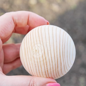 Puede incluir: Una bola de madera lisa y blanca con textura acanalada. La bola tiene un di&aacute;metro de aproximadamente 5 cm.