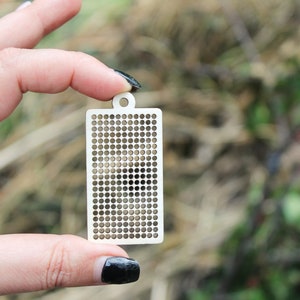Peut inclure: Un pendentif rectangulaire en bois clair pr&eacute;sentant une grille de petites d&eacute;coupes circulaires r&eacute;guli&egrave;rement espac&eacute;es. Le pendentif poss&egrave;de un petit trou circulaire au centre sup&eacute;rieur pour la fixation, avec un design d&eacute;coup&eacute; au laser.