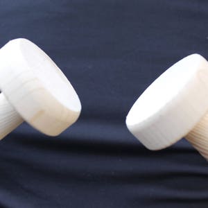 Puede incluir: Dos clavijas de madera con extremos redondeados. Las clavijas son sin terminar y tienen un color de madera natural.