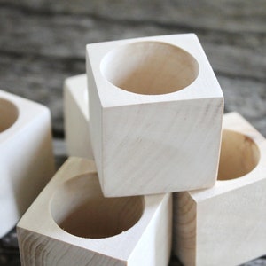 May include: Four unfinished wooden square planters with a round hole in the center. The planters are stacked on top of each other.