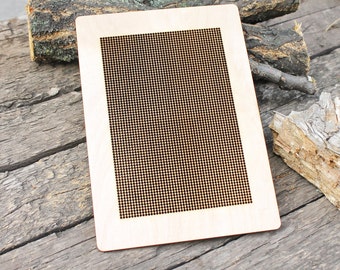 May include: A rectangular light-colored wooden board featuring a large central area filled with a dense, uniform grid of small, dark, circular perforations. The board has smooth, rounded corners and a flat surface, contrasting with the natural wood grain.