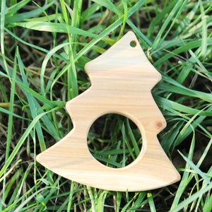 May include: A wooden Christmas tree ornament in the shape of a tree with a hole in the center. The ornament is light brown and is sitting on a bed of green grass.