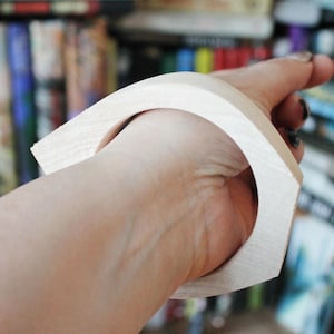 May include: A white wooden bangle bracelet with a curved shape. The bracelet is worn on a person's wrist.