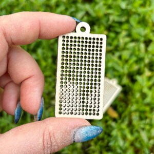 Peut inclure: Un pendentif rectangulaire en bois clair pr&eacute;sentant une grille de petites d&eacute;coupes circulaires r&eacute;guli&egrave;rement espac&eacute;es. La pi&egrave;ce poss&egrave;de un petit trou circulaire en haut pour la suspension et une surface lisse et plate avec un grain de bois naturel.