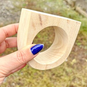 May include: A thick, light-colored wooden ring with a smooth, unfinished surface and a wide, flat top edge. The ring features a circular opening in the center and a natural wood grain pattern visible throughout the exterior and interior surfaces.
