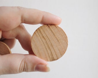 May include: A close-up of a hand holding a round, wooden disc. The disc has a natural wood grain pattern and is smooth to the touch.