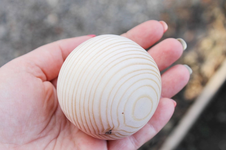 Puede incluir: Una bola de madera blanca con un patr&oacute;n de c&iacute;rculos conc&eacute;ntricos. La bola est&aacute; siendo sostenida en la mano de una persona.