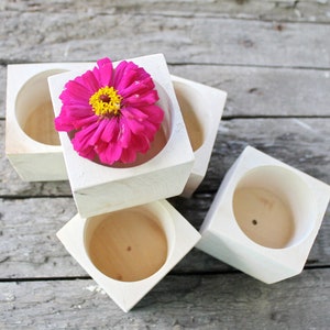 May include: Four white wooden square planters with a pink flower in the top planter.