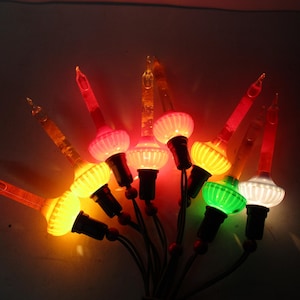 Może przedstawiać: Grupa zabytkowych lampek choinkowych z kolorowymi żarówkami. Żarówki są w różnych kolorach, w tym czerwonym, żółtym, zielonym i białym. Lampki mają klasyczny, retro design.