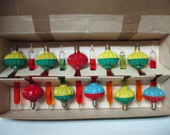 May include: A set of vintage Christmas bubble lights in a cardboard box. The set includes several glass bulbs with colorful liquid-filled chambers in red, yellow, green, and blue, featuring metallic bases and clear glass tubes with colored liquid.