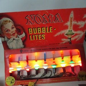 May include: A vintage Noma Bubble-Lites Christmas light set in a red cardboard box. The box features a graphic of a child dressed as Santa Claus and text reading Noma Bubble-Lites. Inside, nine colorful bubble lights are illuminated in a row.