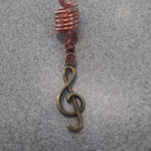 May include: A copper wire hair wrap with a treble clef charm. The hair wrap is coiled and the charm is attached to the bottom of the wrap.