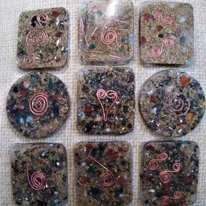 Op de afbeelding: Negen vierkante onderzetters van hars met ingebedde glitter en koperdraadontwerpen. Elke onderzetter heeft een uniek spiraalpatroon.