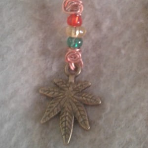 May include: A copper wire hair cuff with a spiral design and a dangling marijuana leaf charm. The charm is decorated with red, yellow, and green beads.