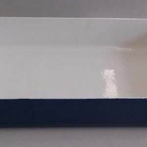 May include: A rectangular baking dish with a deep navy blue exterior and a smooth, glossy white interior. The vessel features integrated handles on both short ends, with a textured, mottled finish on the top surface of the handle grips.
