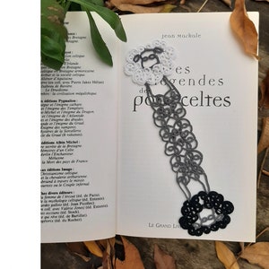 May include: A black and white tatting pattern bookmark with a sheep design. The bookmark is laying on a book titled "Les Grandes Legendres des Celtes" by Jean Markale. The bookmark is surrounded by fallen leaves.