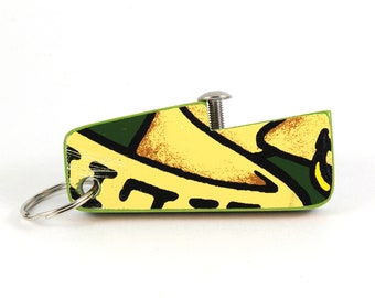 May include: A yellow, green, and brown patterned bottle opener with a silver screw and a silver key ring.
