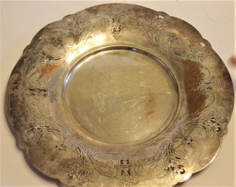 May include: A silver serving platter with an ornate, engraved design of floral motifs. The platter has a scalloped edge and a raised rim.