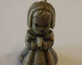May include: A small, green, wax figurine of a girl wearing a dress and a bonnet. The figurine has a simple, childlike face with black eyes and a small mouth.