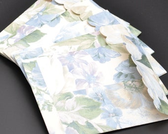 May include: A stack of paper envelopes featuring a floral pattern in shades of light blue, sage green, and cream. Each envelope has a scalloped flap edge and is constructed from paper with a printed botanical design of flowers and leaves.
