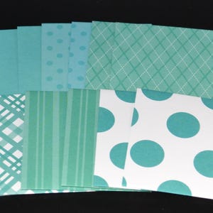 May include: A collection of square paper sheets in various shades of teal and white. The patterns include solid teal, teal polka dots, a white grid on teal, a white plaid pattern on teal, vertical teal stripes, and large teal polka dots on white.