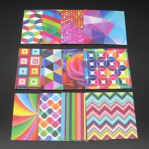 May include: A collection of twelve rectangular cards featuring diverse colorful patterns including geometric cubes, rainbow stripes, polka dots, abstract polygons, squares, triangles, a rose, floral motifs, sunburst rays, hearts, and chevron zigzags.