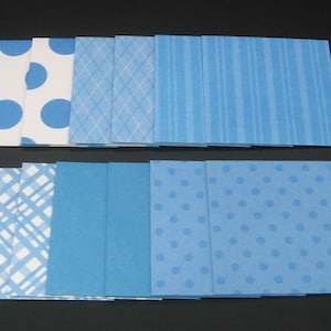 May include: A collection of square paper sheets in various shades of blue, featuring patterns including large polka dots, thin white diamond grids, vertical stripes, blue and white plaid, solid blue, and small light blue polka dots on a blue background.