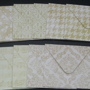 May include: A collection of nine square paper envelopes featuring various patterns in shades of beige and cream. The designs include houndstooth, floral motifs, geometric diamond shapes, and musical notation prints, all with triangular flaps.