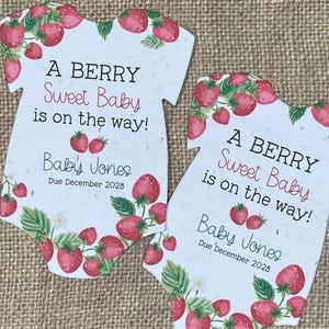 May include: Two baby announcement cards shaped like onesies. Each card features a strawberry design and the text "A BERRY Sweet Baby is on the way!" with the name "Baby Jones" and the due date "December 2028".