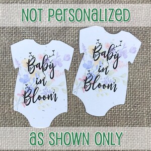 K&ouml;nnte beinhalten: Zwei wei&szlig;e Baby-Bodys mit einem Aquarell-Blumenmuster und dem Text "Baby in Bloom".