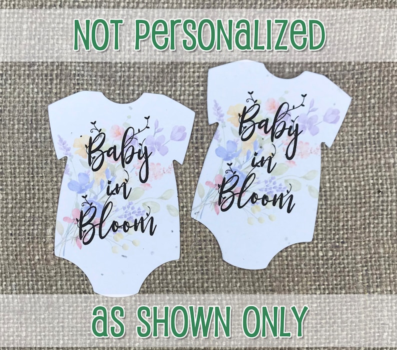 K&ouml;nnte beinhalten: Zwei wei&szlig;e Baby-Bodys mit einem Aquarell-Blumenmuster und dem Text "Baby in Bloom".