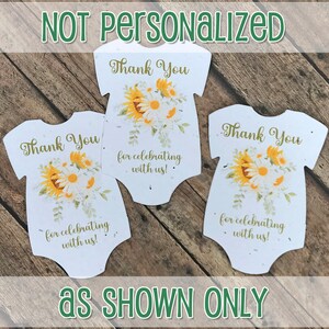 K&ouml;nnte beinhalten: Drei wei&szlig;e Baby-Strampler-f&ouml;rmige Dankeskarten mit einem Sonnenblumen- und G&auml;nsebl&uuml;mchen-Blumendesign. Der Text auf den Karten lautet "Vielen Dank f&uuml;rs Feiern mit uns!"