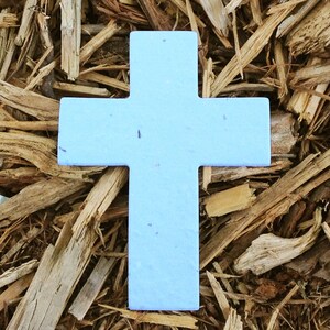 May include: A light blue wooden cross, made of recycled materials, sits on a bed of brown wood chips.