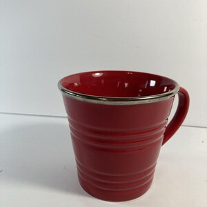 May include: A red ceramic mug with a silver rim and handle. The mug has horizontal ridges around the body. Suitable for tea, coffee, or other drinks.