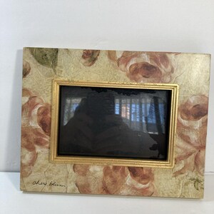 Peut inclure: Cadre photo rectangulaire avec un cadre intérieur doré et un motif floral. Le cadre a un fond crème avec de grandes roses roses et pêche fanées. La signature de l'artiste, "Cheri Blum", est visible en bas à gauche.