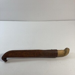 May include: A brown knife with a curved blade and a wooden handle. The knife is in a brown leather sheath with carved geometric designs. The sheath is approximately 10 inches long.