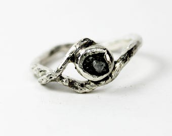 May include: A silver ring with a rough, natural diamond set in a twisted band.
