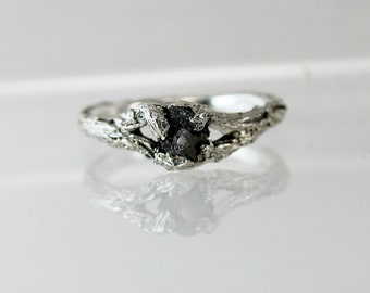 May include: A silver ring with a rough, black diamond set in a branch-like design.