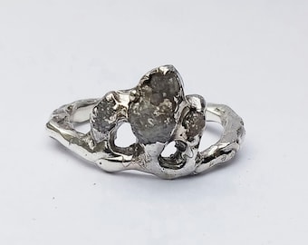 May include: A silver ring with a large, rough, grey gemstone set in a unique, organic, branch-like design.