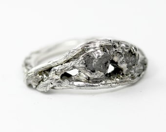 May include: A silver ring with a rough, organic design featuring two grey diamonds set in the center.