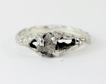 May include: A silver ring with a rough, natural diamond set in a textured band.